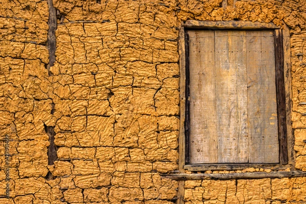 Fototapeta Detail of a traditional rammed earth wall with a rustic wooden window. The cracked texture reveals the beauty of this vernacular building technique.
