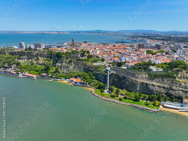 Fototapeta Riverside village and buildings below the Almada cliffs with a tall glass elevator connecting to the city above