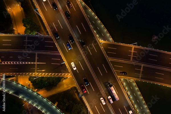 Fototapeta Aerial view of a busy road junction during nighttime with illuminated highways and moving vehicles.