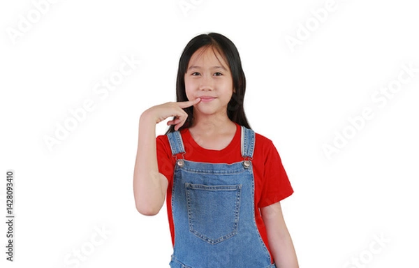 Fototapeta Portrait of smiling Asian girl kid hold finger at mouth while standing and looking at you isolated on white studio background.