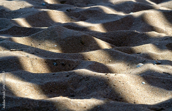 Fototapeta Sunny natural background with sand and shells. A striped shadow falls on the undulating mounds of sand.