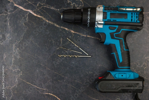 Obraz A modern power drill and screws on a dark textured surface, ideal for DIY and home improvement projects.