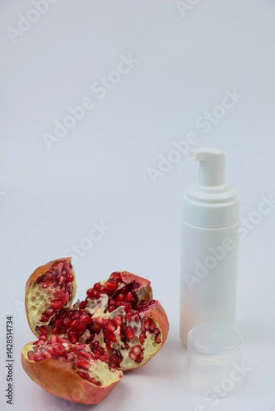 Obraz A beautiful pomegranate placed next to a white skincare pump bottle resting on a simple, plain background