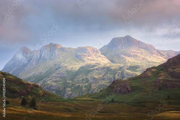 Fototapeta A dramatic morning in the Lake District, where golden sunlight bathes the rugged Langdale Pikes, casting a serene glow over the majestic landscape.