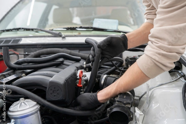 Fototapeta Mechanic works on installing air hose inside the engine compartment of a vehicle, ensuring proper function at an auto repair shop.