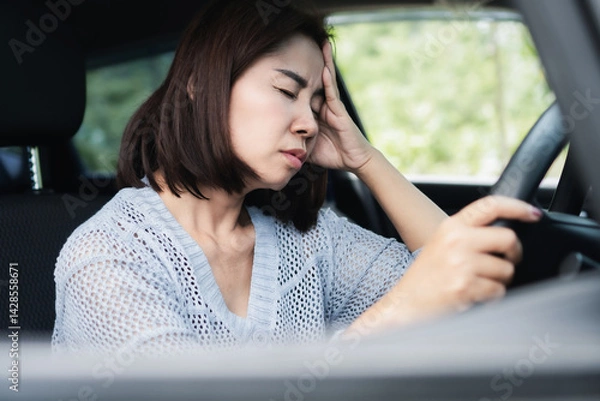 Obraz Asian woman feeling sick, dizzy, and having a headache while driving, stopping the car to rest and take a break after a long drive to stay safe and avoid accidents