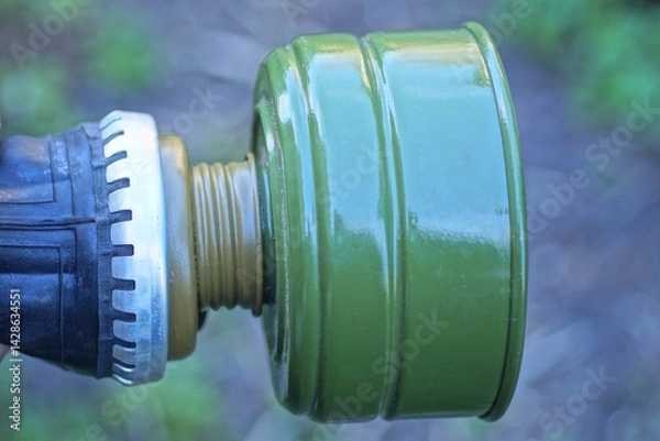 Obraz one green old round metal filter from a gas mask lies on a gray background on a summer street