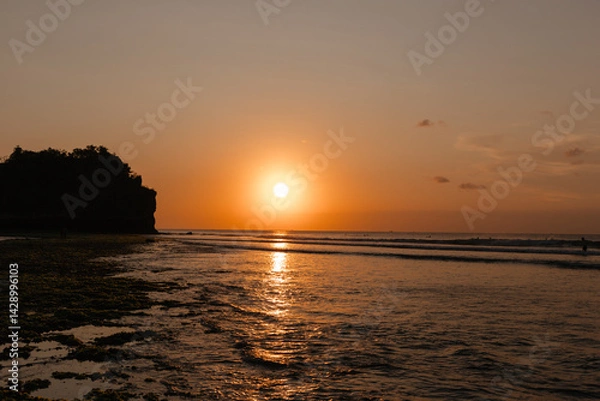 Fototapeta Bright orange sun at sunset against the background of the ocean. View from the beach to the evening sun and waves