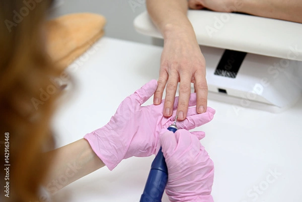 Fototapeta The manicure master performs a hardware manicure for the client in pink latex gloves, ensuring careful nail care so that they look flawless. Close-up of women's hands, hardware manicure