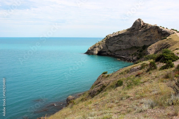 Fototapeta Rocky coastline meeting turquoise water under cloudy sky