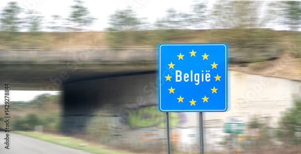 Obraz Road sign on the highway indicating the border of a country in the European Union: Belgium. Written in Dutch - Belgium. Concept of entry restrictions into the EU and border checks. Blurred motion.