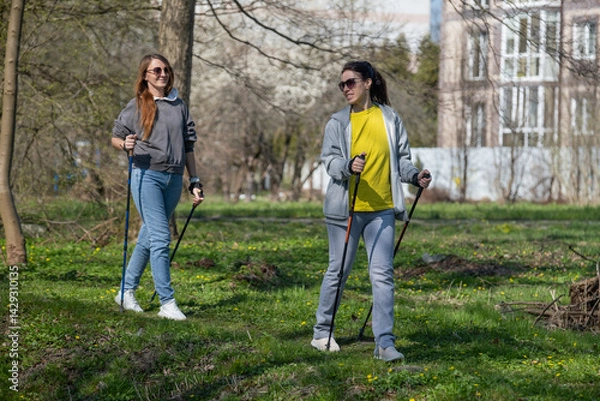 Fototapeta two women walking in the forest with sticks, Nordic walking, lesbians doing sports, couple in love	