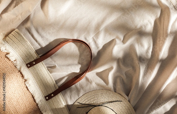 Fototapeta Summer essentials on linen tablecloth background. Flat lay of straw hat and bag in gentle sunlight. Copy space for product. Boho summer vibes. 