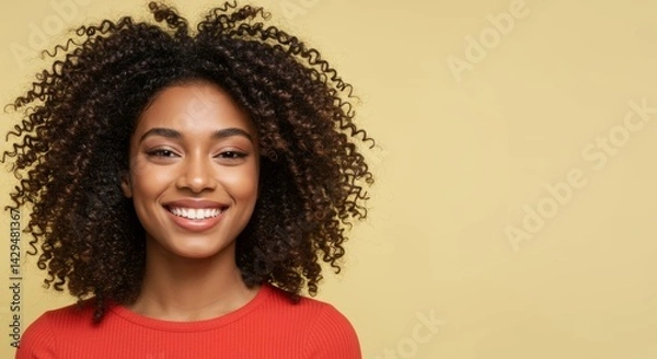 Fototapeta Smiling young woman with curly hair, wearing a red top, set against a soft yellow background, exuding happiness and confidence
