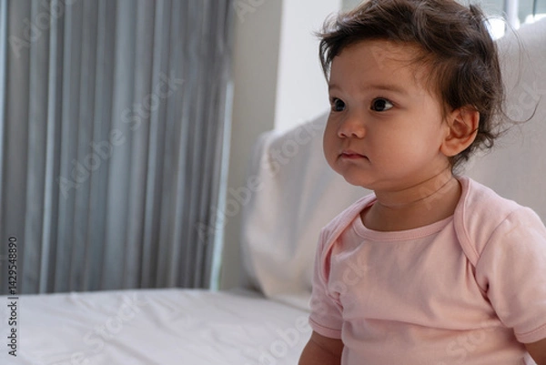Obraz Lovely healthy little infant daughter sitting alone looking at something at home. Happy nice innocence asian mixed race kid looking at family sitting in room. Adorable joy children girl sitting alone.