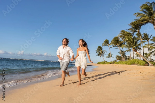 Fototapeta Happy couple relaxing running together having fun during sunset on tropical beach. Summer travel destination.