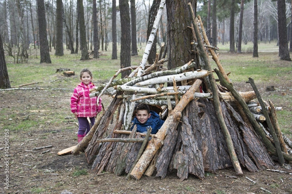 Fototapeta In the spring in a pine forest, a brother with a small sister built a hut of sticks.