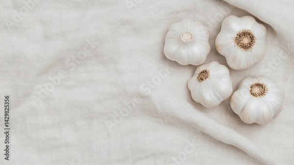 Fototapeta Four garlic bulbs arranged on a textured, neutral fabric background, showcasing their unique shapes and details.