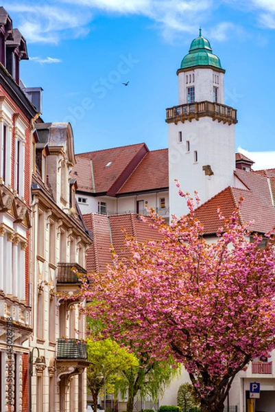 Obraz The “Altes Stadtbad“ (Old city baths) is a historic building in the city of Iserlohn (Germany). The monuments tower and facade have been preserved. Street in spring season with blooming cherry trees.