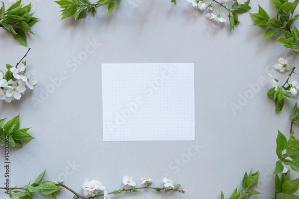 Fototapeta Spring background with paper sheet. Beautiful fresh flowers and leaves on gray background