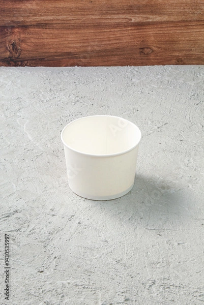 Fototapeta Empty White Paper Bowl on Concrete Textured Table with Wooden Background, Rustic Minimalist Kitchen Scene for Food Mockup or Tableware Display with Copy Space