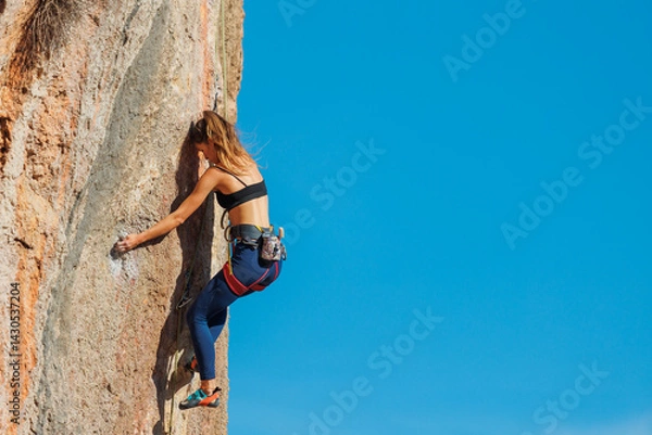 Fototapeta The girl climbs the rock. The climber is training to climb the rock. A strong athlete overcomes a difficult climbing route. Extreme hobby. .