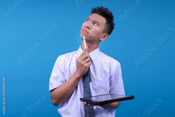 Obraz Pensive Young Asian Student Man Thinking With Hand On Chin While Using Digital Tablet