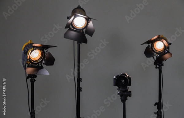 Fototapeta Digital SLR camera and three spotlights with Fresnel lenses. Manual interchangeable lens for filming. Shooting in the interior with artificial light. Equipment for movies.