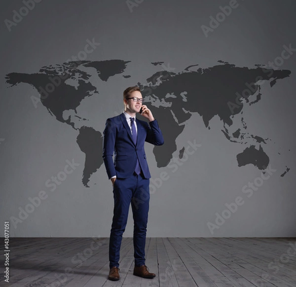 Fototapeta Businessman standing with smartphone. World map background. Business, globalization, concept.