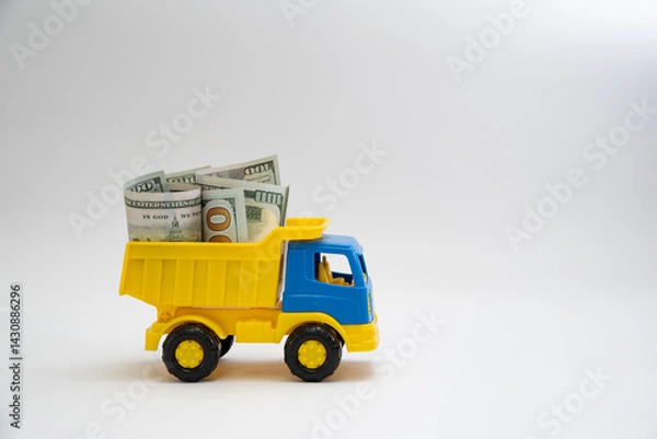 Fototapeta Dollar bills are transported by a yellow and blue toy car on a white background.
