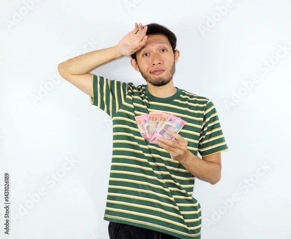 Fototapeta Man Holding Money Showing Uncertain Expression About Financial Situation