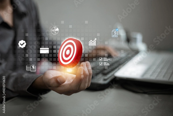 Fototapeta A person holding a floating 3D target symbol in their palm surrounded by business and financial icons, symbolizing business objectives and achievement.