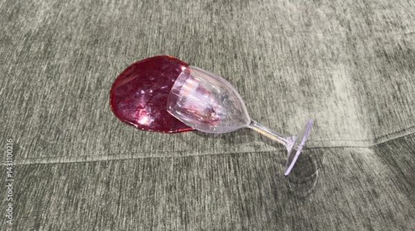 Fototapeta A glass of red wine has tipped and spilled onto a green fabric sofa, creating a large stain with visible splash marks and soft reflections on the upholstery