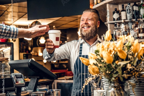 Obraz A man selling coffee to a consumer in a coffee shop.