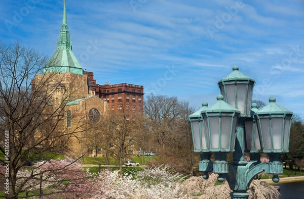 Fototapeta A church in the University Circle district of Cleveland Ohio stands above flowering cherry trees and an ornamental lamp post on a bright spring morning.