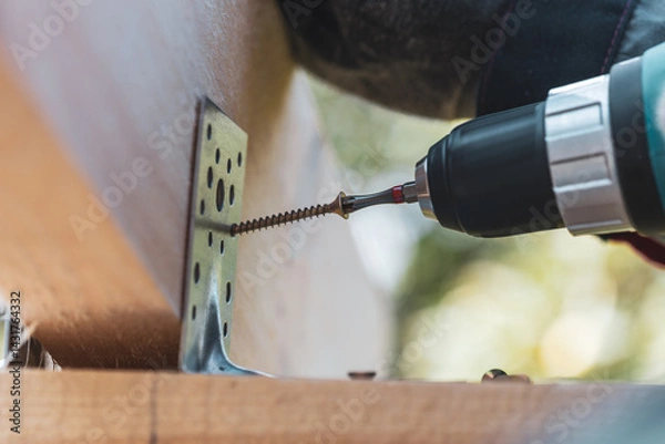 Fototapeta An electric screwdriver screws a self-tapping screw into the wood