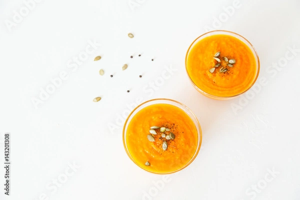 Fototapeta Two plates of pumpkin soup with seeds on a white background with space for your text.
