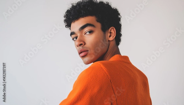Obraz Pensive Gaze: A Portrait of a Young Man in his Early 20s, Wearing an Orange Crew Neck Sweatshirt, Against a Neutral Background.  The image captures a thoughtful expression and a subtle intensity in