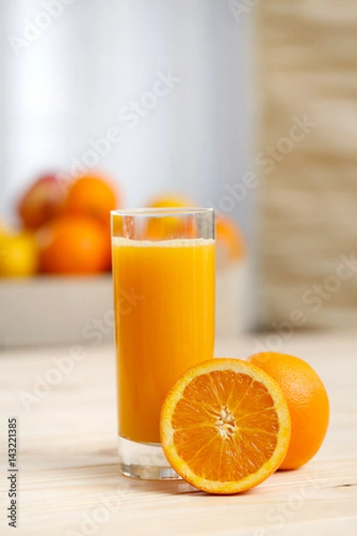 Fototapeta Orange juice in a tall glass with an orange half And basket of fruit in the background