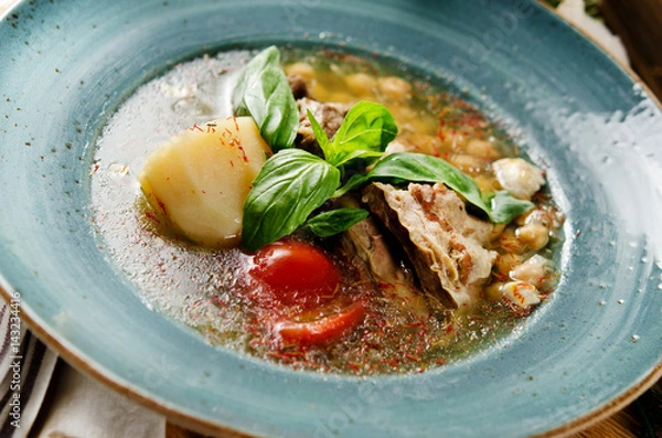 Obraz Soup with mutton broth with mutton meat, rice, chickpeas, potatoes, carrots, bell peppers, tomatoes, greens and oriental spices