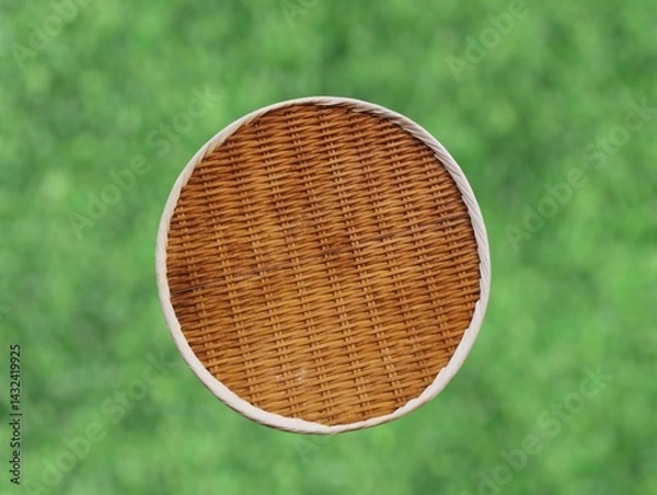 Fototapeta The background of the picture is a blurred image of a green lawn. In the picture is a finely woven bamboo and rattan winnowing basket or tray with a rim and is lightweight and can be used to hold food