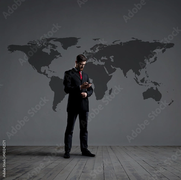 Fototapeta Businessman standing with smartphone. World map background. Business, globalization, concept.