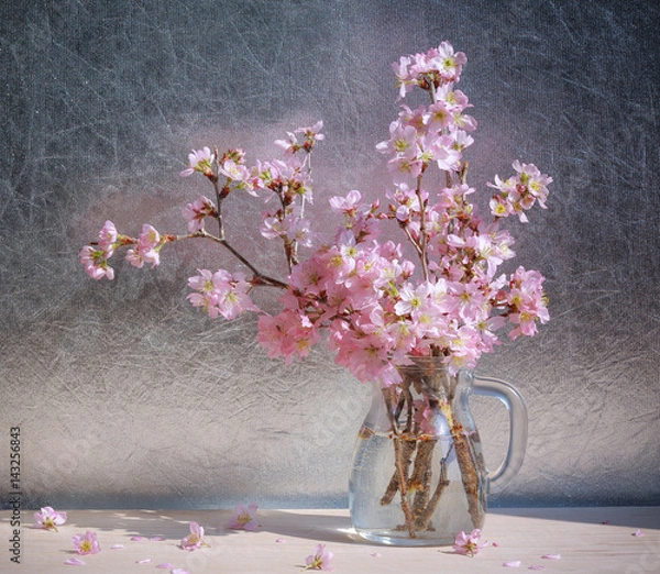Obraz Pink  cherry blossoms in vase on wooden table in the sunlight.
