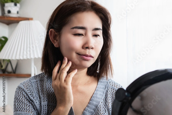 Obraz asian woman struggling with bell's palsy or facial palsy, showing facial weakness and a drooping mouth, holding her face while checking in the mirror, possibly caused by viral infections or stress