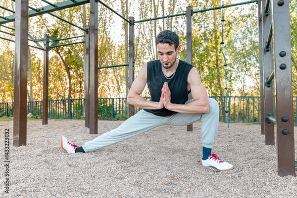 Obraz Athletic man in Cossack squat stretch outdoors, improving lower body mobility, hip flexibility, and joint control in a gravel-surfaced calisthenics area
