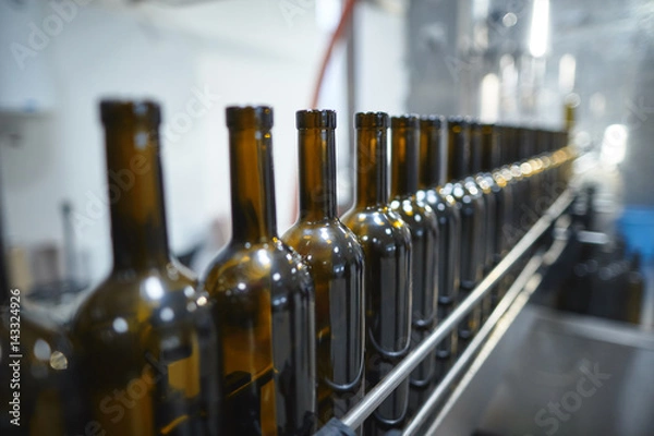Fototapeta Row of glass wine bottles moving by conveyor