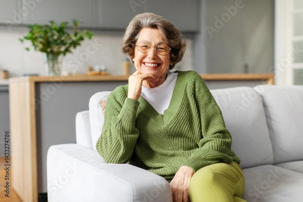 Fototapeta Portrait of happy senior woman relaxing on comfortable couch at home, sitting on sofa, looking and smiling at camera, enjoying retirement time