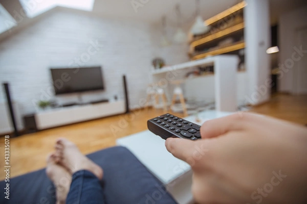 Obraz Close up and part of human hand using remote control on sofa in living room