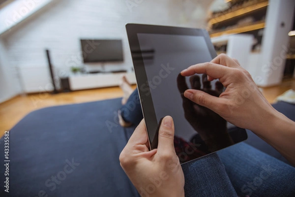 Obraz Close up and part of human hand using digital tablet on sofa in living room