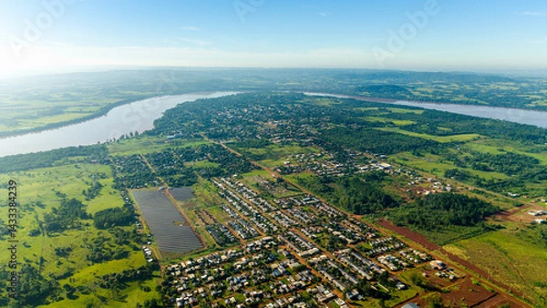 Obraz Aerial view of a large solar park surrounded by greenery, with a town in the background.